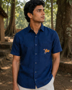 Sohrai Jeev Dhara hand-painted linen shirt in a forest setting, featuring a solitary peahen painted on the chest pocket.