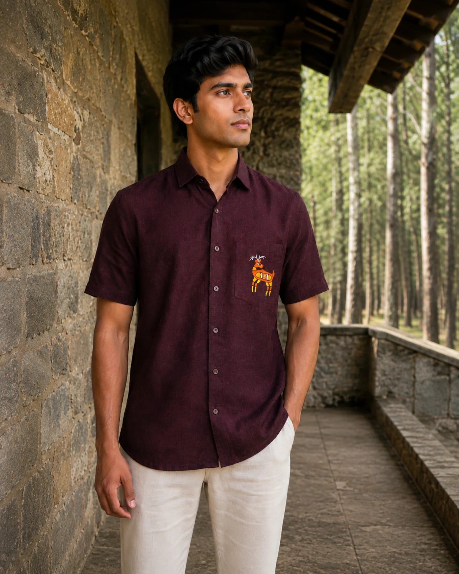 Sohrai Jeev Pravah hand-painted linen shirt featuring a solitary deer on the chest pocket, photographed along a stone gallery overlooking woodland.