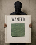 Masked figure holding a weathered white “WANTED” sign displaying a folded, hand-hemmed Forest Moss khadi handkerchief.