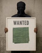 Masked figure holding a weathered white “WANTED” sign displaying a folded, hand-hemmed Forest Moss khadi handkerchief.