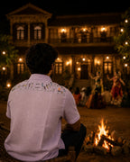 Warli aabha hand-painted linen shirt featuring a back-yoke composition of warli dancers, animals, musicians and a ceremonial fire, observed during a Lavani performance in the courtyard of a historic Maharashtrian villa beside a traditional wood fire at night.