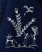 Warli Aavartan hand-painted linen shirt right shoulder close-up featuring flowering plants, a flying bird, horned animal, a male figure carrying a stick around his neck, and a female figure carrying a basket for the crop yield.