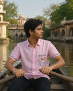 Warli Matsya hand-painted linen shirt featuring a fishing-boat pocket artwork and dancing-figure sleeve borders, worn while rowing a private wooden boat through a palace river canal in soft natural daylight.