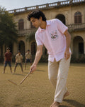 Warli Saanjh hand-painted linen shirt featuring a pocket artwork depicting village life through flowering plants, birds, a sun artwork, and basket-carrying figures, observed during a game of gilli danda in the courtyard of a heritage residence, with village children softly blurred in the background.