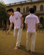 Warli Saanjh hand-painted linen shirt shown in a styled context featuring front and back views, with flowering plants, sun, birds and human figures on the pocket, and a hand-painted Warli narrative artwork across the back, photographed during a game of gilli danda in a heritage courtyard.