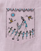 Warli Ullas hand-painted linen shirt pocket close-up featuring a traditional Tarpa dance scene with a tarpa musician leading a circle of dancers beneath sunlight, accompanied by birds and decorative warli borders, painted directly on linen fabric.