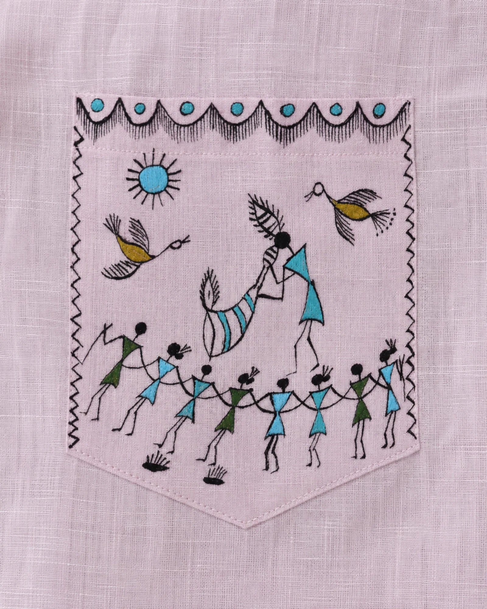 Warli Ullas hand-painted linen shirt pocket close-up featuring a traditional Tarpa dance scene with a tarpa musician leading a circle of dancers beneath sunlight, accompanied by birds and decorative warli borders, painted directly on linen fabric.