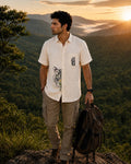 Padchinh hand-painted linen shirt featuring tiger artwork crossing the front placket and botanical detailing above the pocket, photographed on a mountain ridge above a forested valley in warm evening light.