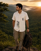 Padchinh hand-painted linen shirt featuring tiger artwork crossing the front placket and botanical detailing above the pocket, photographed on a mountain ridge above a forested valley in warm evening light.