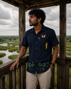 Vanantara hand-painted linen shirt featuring butterfly artwork across the upper front, tiger artwork beside the pocket and botanical artwork along the lower front panel, photographed from a marshland watchtower.