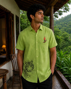 Vanchar hand-painted linen shirt featuring tiger artwork on the lower front panel and a woodpecker perched on a botanical branch above the pocket, photographed at a jungle lodge overlooking a forested hillside in natural light.