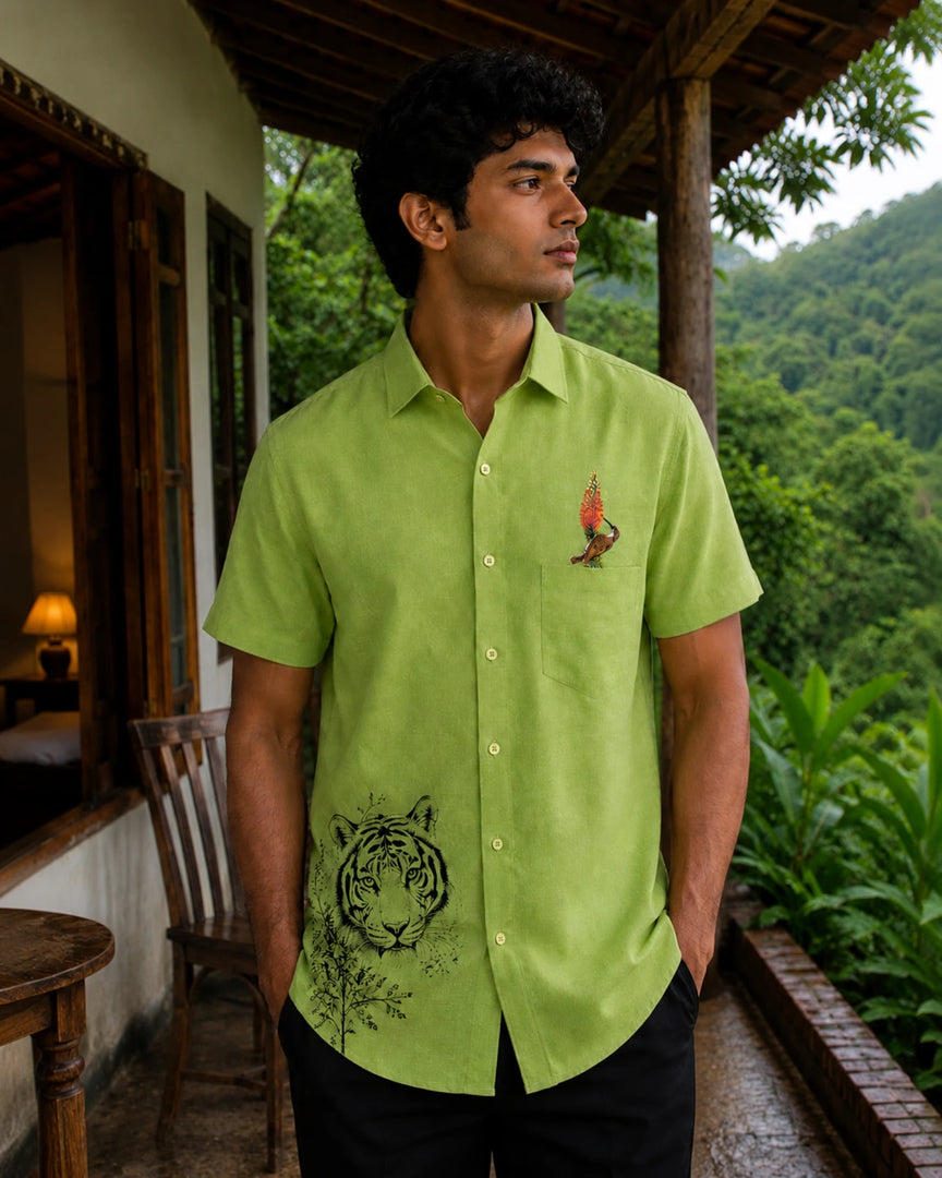 Vanchar hand-painted linen shirt featuring tiger artwork on the lower front panel and a woodpecker perched on a botanical branch above the pocket, photographed at a jungle lodge overlooking a forested hillside in natural light.