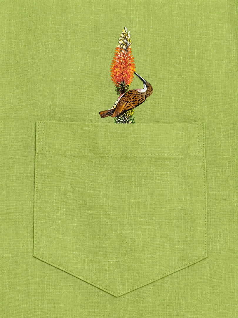 Woodpecker perched on a botanical branch above the pocket of the Vanchar hand-painted linen shirt.