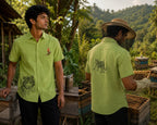 Front and back styled context view of the Vanchar hand-painted linen shirt, featuring tiger artwork on the lower front panel and a woodpecker perched on a botanical branch above the pocket, with a walking tiger artwork on the back, photographed at a beehive farm surrounded by forested hills.